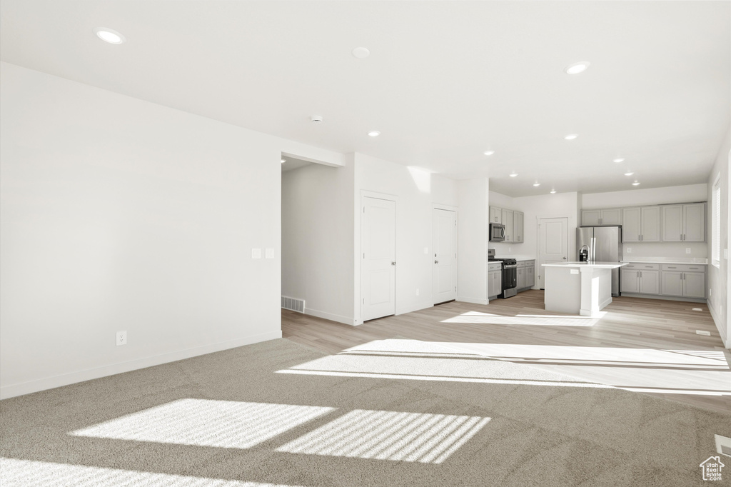 Unfurnished living room with recessed lighting, light colored carpet, and light wood-style floors
