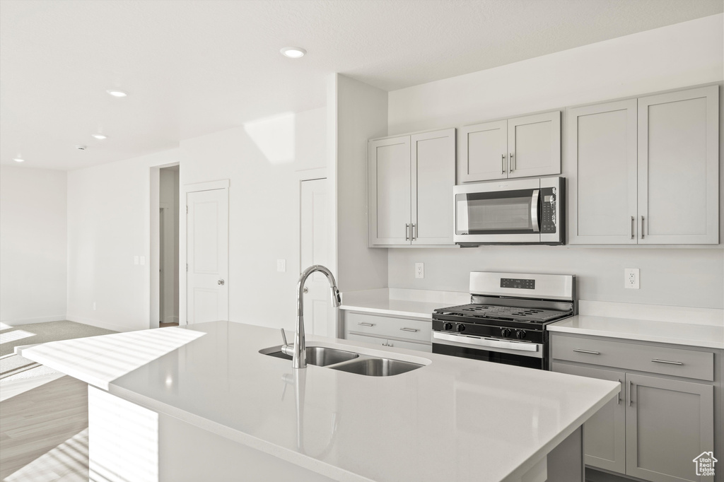 Kitchen with appliances with stainless steel finishes, gray cabinetry, recessed lighting, light countertops, and a center island with sink