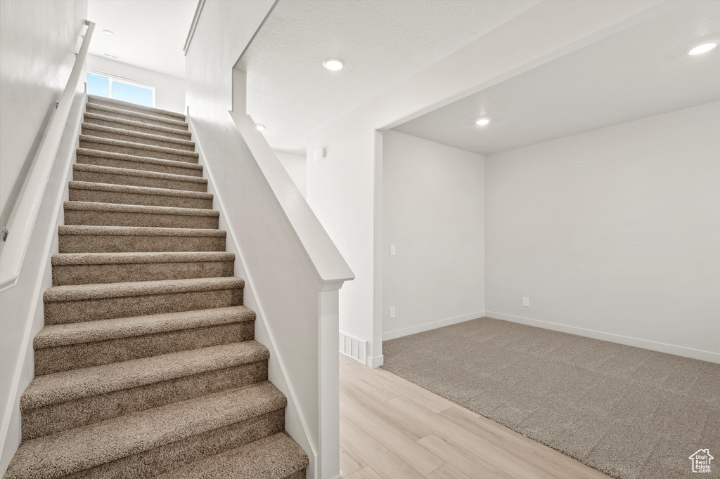 Stairway with wood finished floors, recessed lighting, and carpet floors
