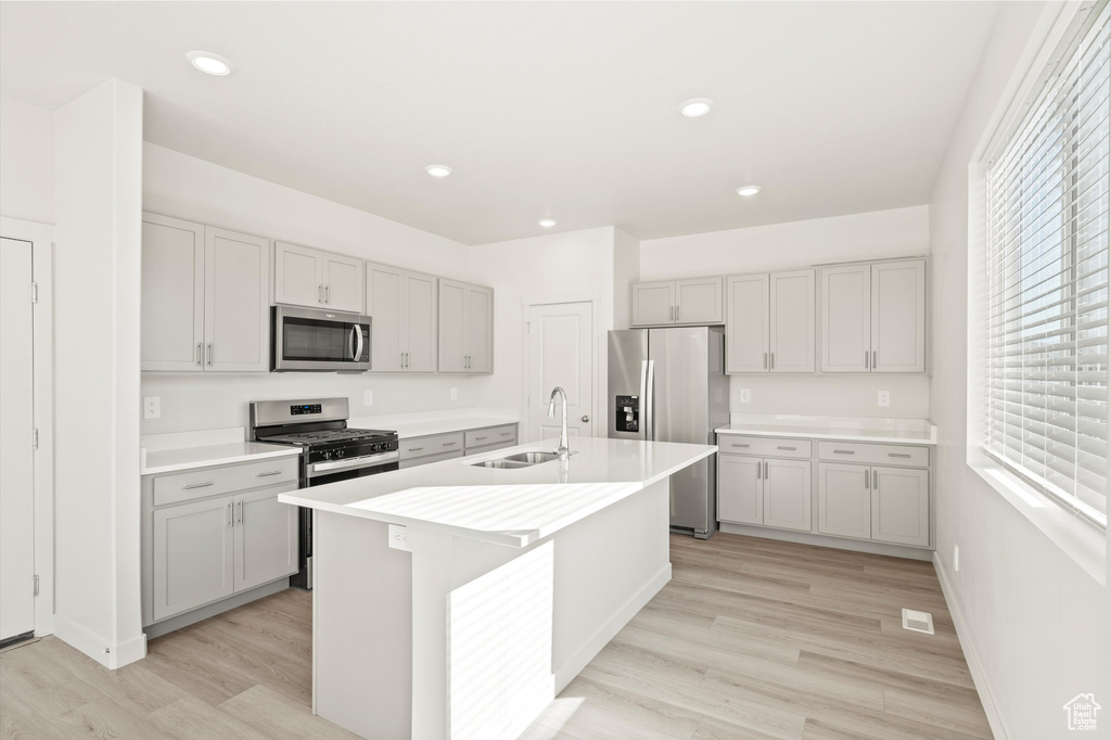 Kitchen featuring stainless steel appliances, light wood-style floors, an island with sink, light countertops, and recessed lighting