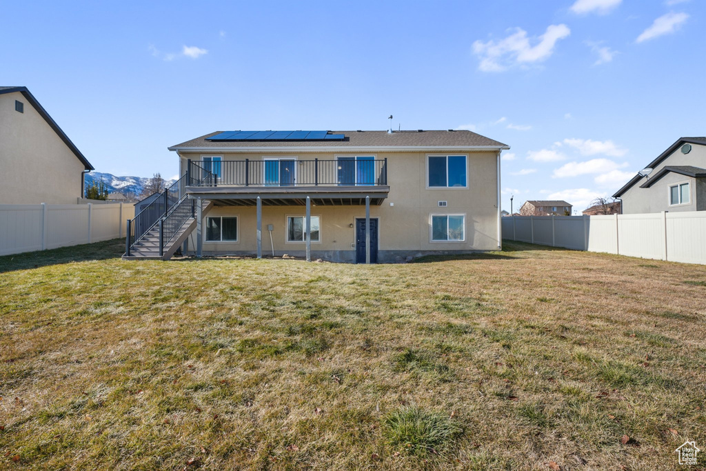 Rear view of house featuring a lawn, a wooden deck, and solar panels