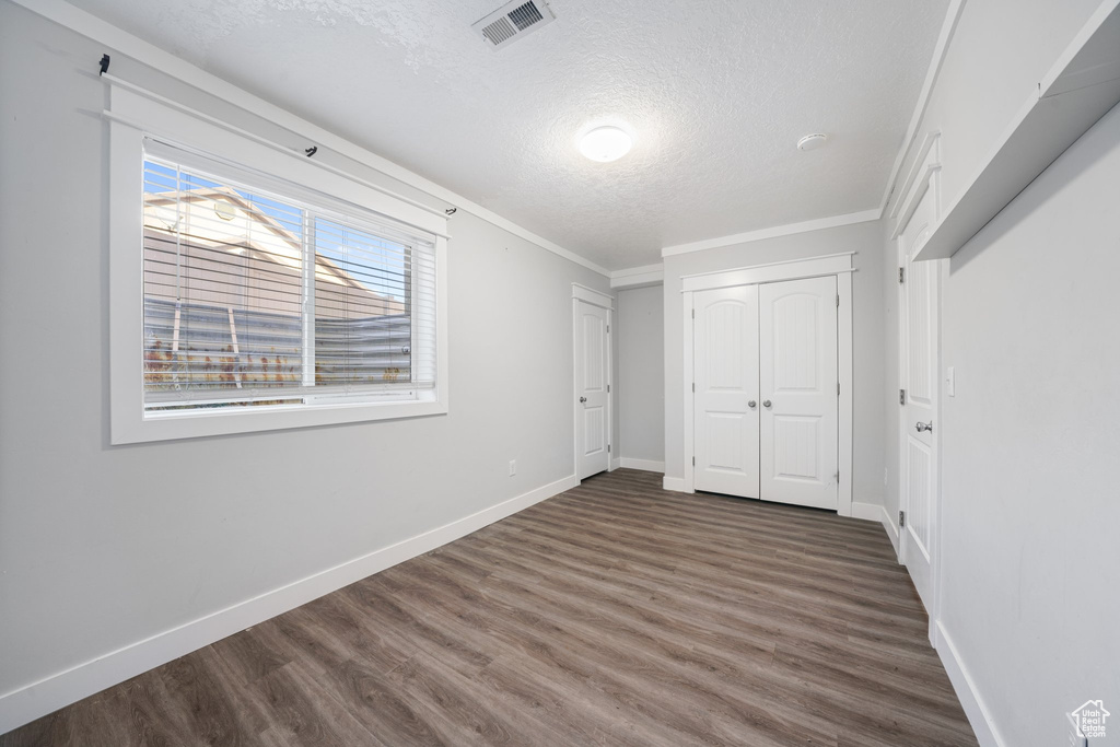 Unfurnished bedroom with a closet, dark wood-type flooring, a textured ceiling, and ornamental molding