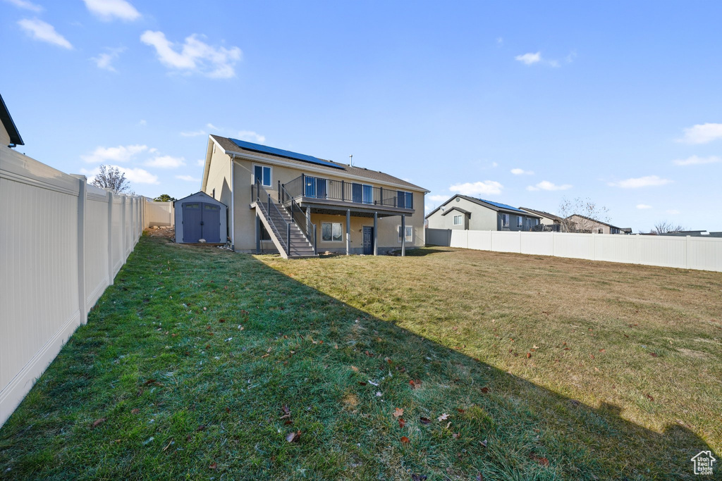 Rear view of house with solar panels, a yard, a deck, and a storage shed
