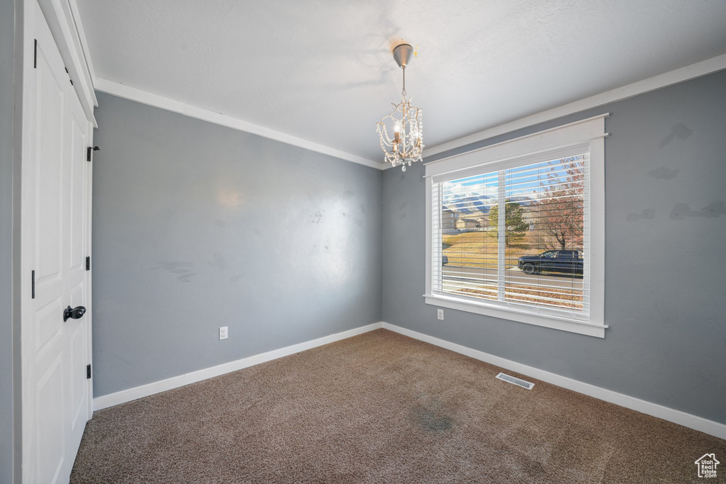 Empty room featuring a notable chandelier, carpet floors, and crown molding