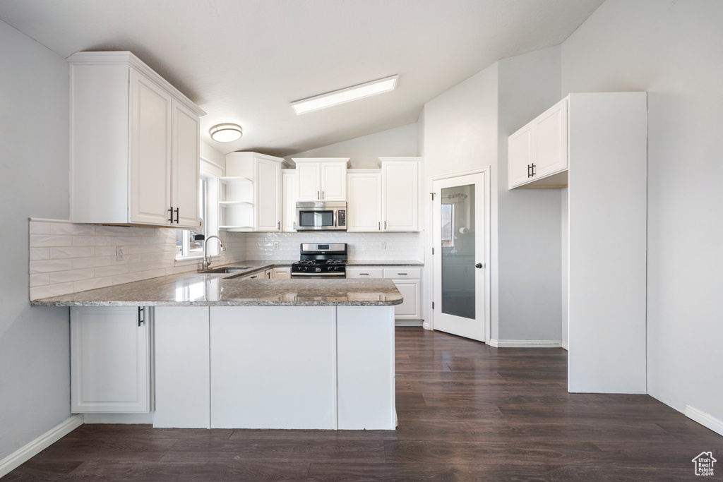 Kitchen featuring kitchen peninsula, stainless steel appliances, vaulted ceiling, sink, and white cabinetry