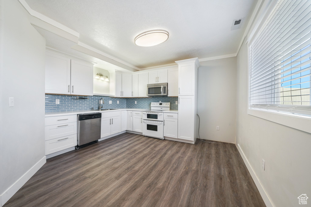 Kitchen featuring dark wood-type flooring, sink, decorative backsplash, white cabinetry, and stainless steel appliances