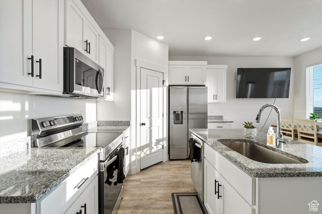 Kitchen with stone counters, sink, an island with sink, white cabinetry, and stainless steel appliances