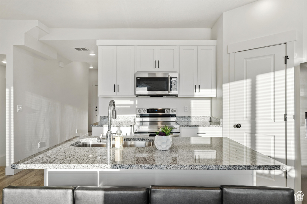 Kitchen featuring light stone countertops, white cabinetry, sink, and appliances with stainless steel finishes