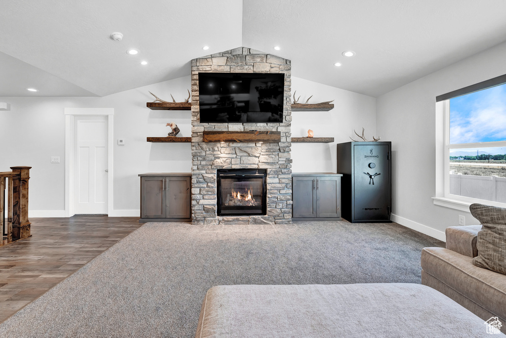 Living room with vaulted ceiling, hardwood / wood-style flooring, and a stone fireplace