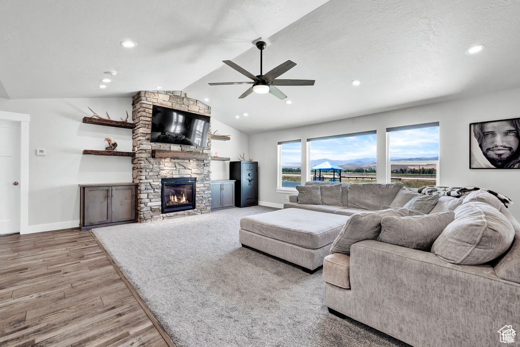 Living room featuring lofted ceiling, a stone fireplace, light hardwood / wood-style flooring, ceiling fan, and a textured ceiling
