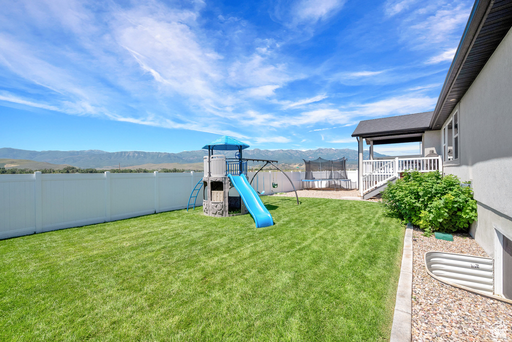 View of play area with a lawn, a mountain view, and a trampoline
