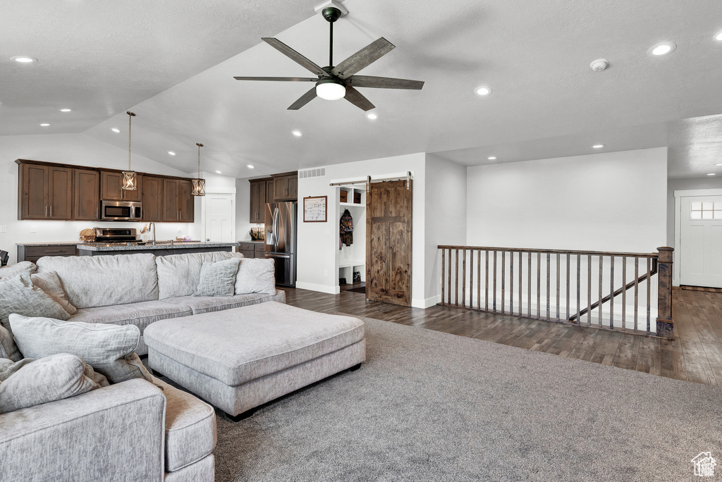 Living room featuring dark hardwood / wood-style flooring, a barn door, ceiling fan, and lofted ceiling
