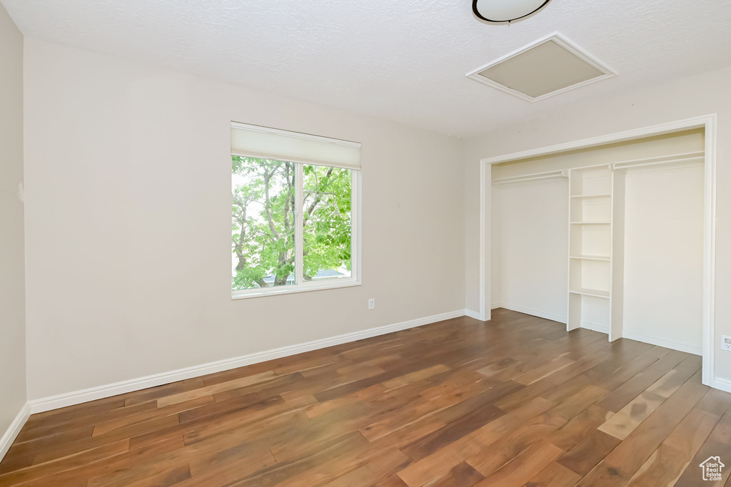 Unfurnished bedroom featuring wood finished floors, attic access, a closet, and baseboards