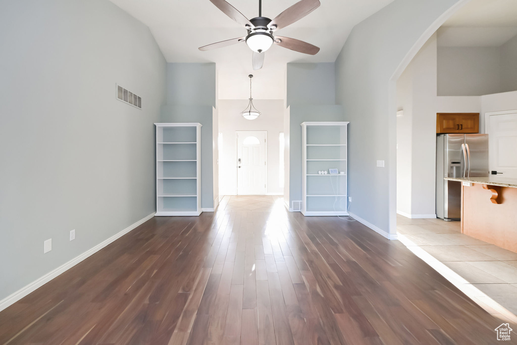 Unfurnished living room with high vaulted ceiling, arched walkways, a ceiling fan, dark wood-style floors, and baseboards