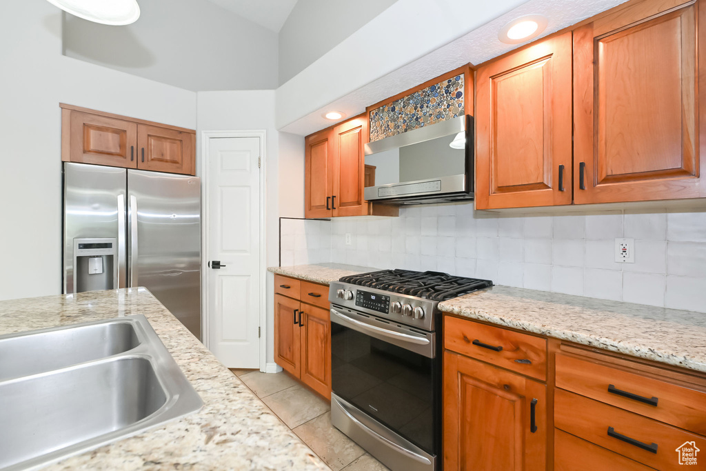 Kitchen featuring appliances with stainless steel finishes, a sink, tasteful backsplash, and brown cabinetry
