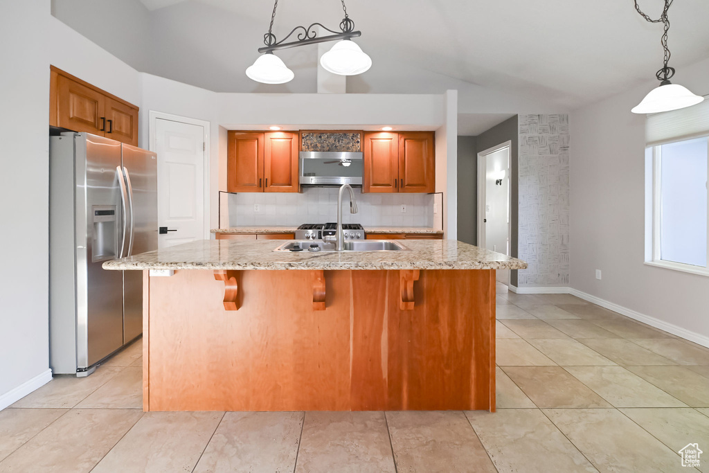 Kitchen with stainless steel fridge with ice dispenser, decorative backsplash, light stone countertops, brown cabinetry, and baseboards