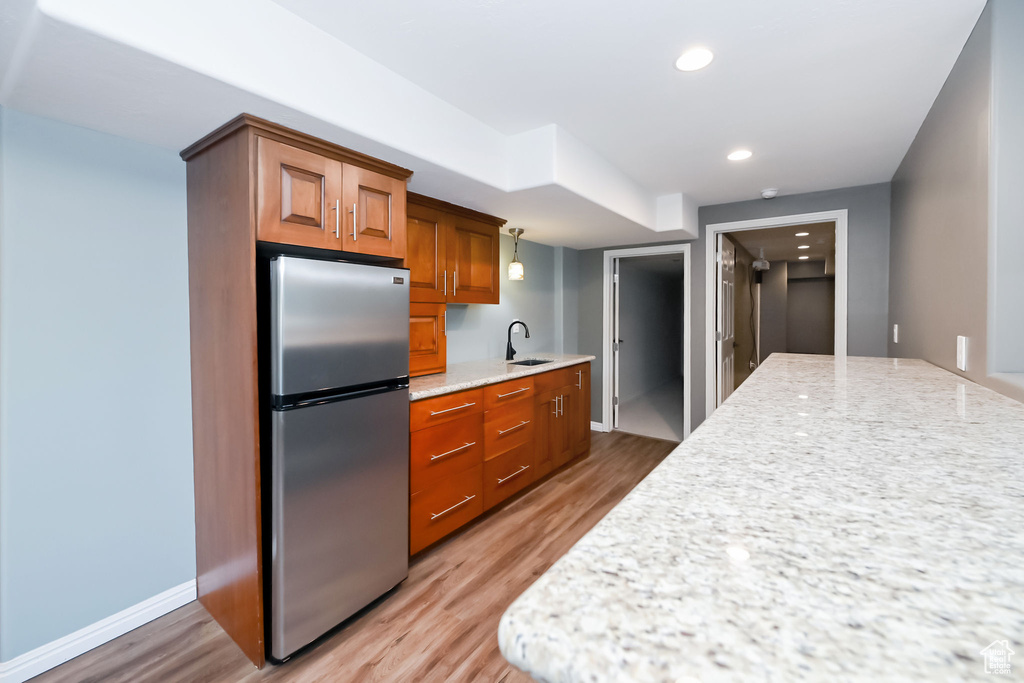 Kitchen featuring freestanding refrigerator, a sink, brown cabinetry, wood finished floors, and light stone countertops