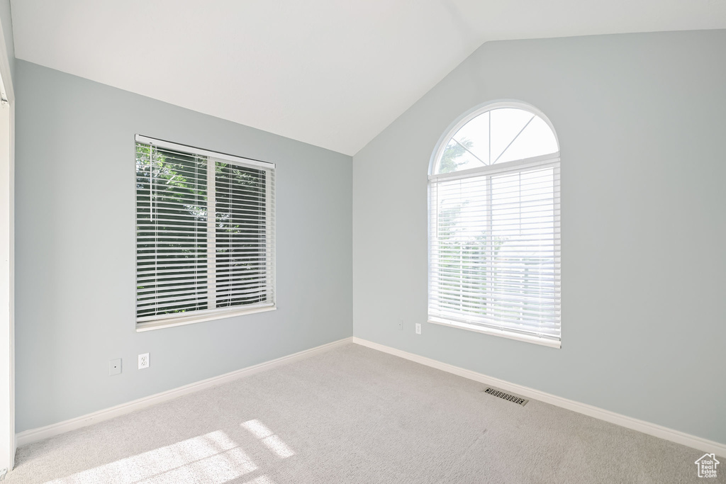 Carpeted empty room featuring vaulted ceiling and baseboards