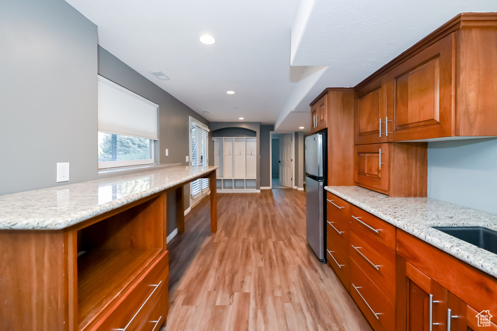 Kitchen with freestanding refrigerator, brown cabinetry, light wood-style flooring, light stone countertops, and recessed lighting
