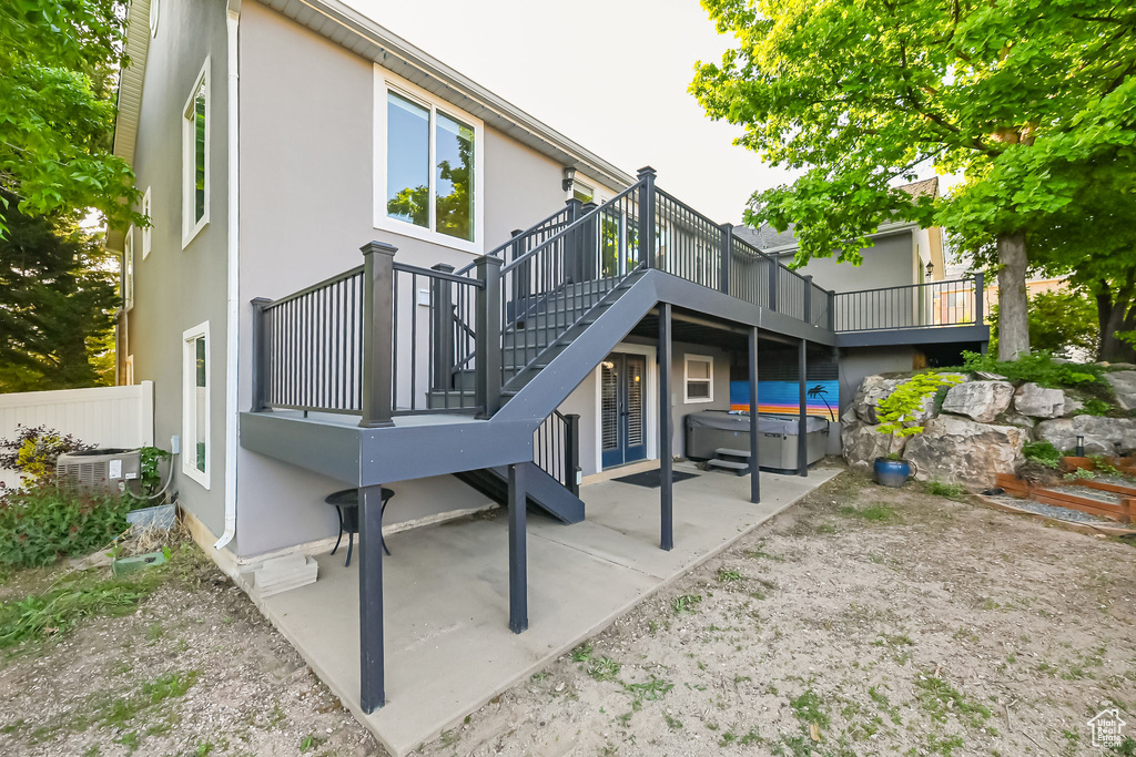 Rear view of property featuring a hot tub, a patio, a wooden deck, stucco siding, and central AC unit
