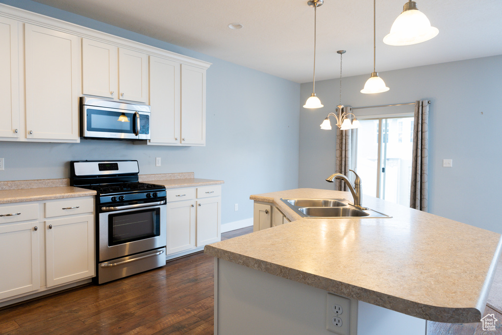 Kitchen with a center island with sink, sink, appliances with stainless steel finishes, decorative light fixtures, and white cabinetry
