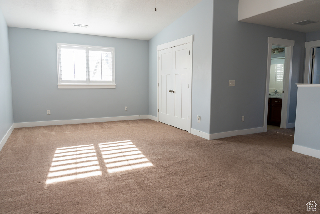 Unfurnished bedroom featuring connected bathroom, light colored carpet, and lofted ceiling