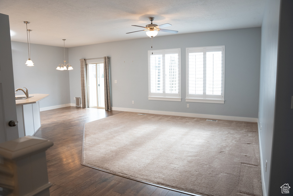 Unfurnished living room featuring dark hardwood / wood-style floors and ceiling fan with notable chandelier