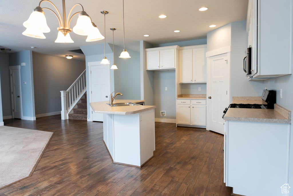 Kitchen featuring white cabinetry, a center island with sink, decorative light fixtures, and sink