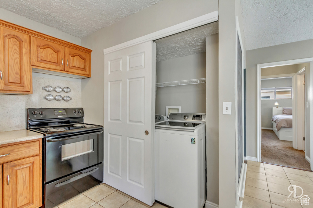 Kitchen featuring black electric range oven, light tile patterned floors, a textured ceiling, and washer / clothes dryer