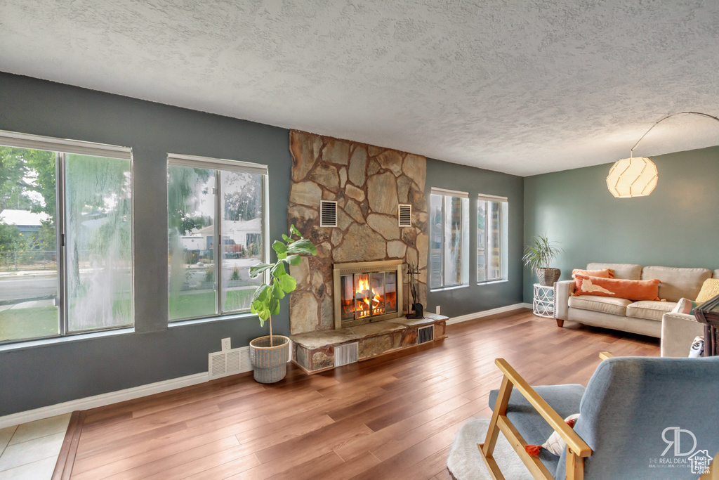 Living room with hardwood / wood-style floors, a textured ceiling, and a stone fireplace