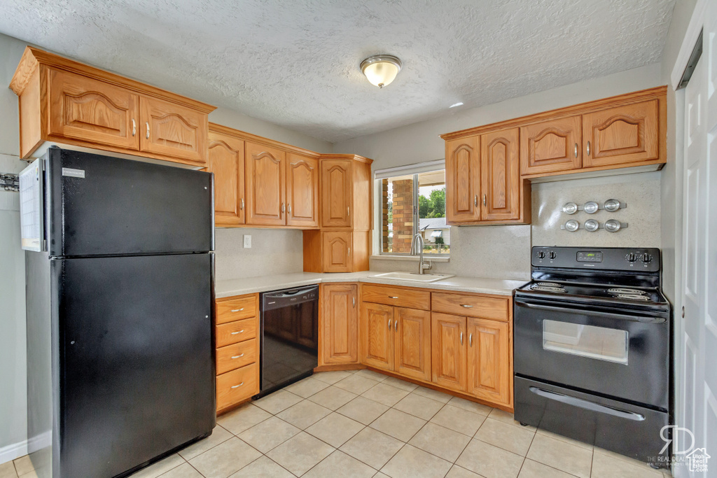 Kitchen featuring sink, backsplash, a textured ceiling, light tile patterned floors, and black appliances