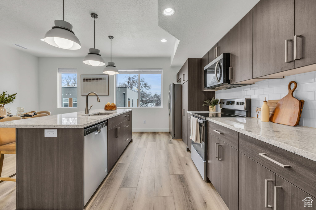 Kitchen with decorative light fixtures, stainless steel appliances, a breakfast bar, a sink, and a center island with sink