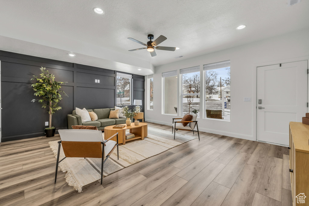 Living area with light wood-type flooring, ceiling fan, a decorative wall, and recessed lighting