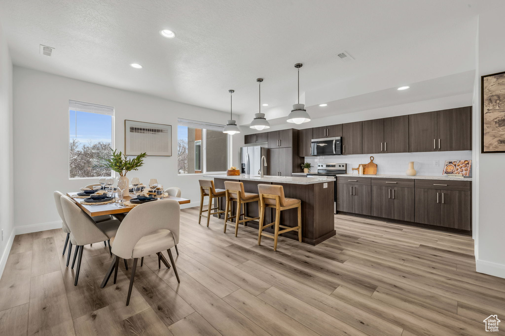 Interior space with pendant lighting, light countertops, stainless steel microwave, dark brown cabinets, and an island with sink