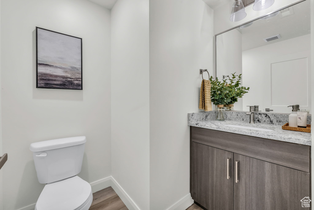 Bathroom featuring visible vents, toilet, vanity, wood finished floors, and baseboards