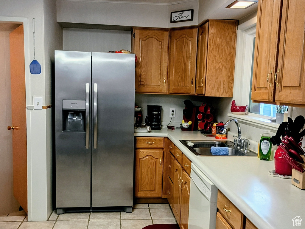 Kitchen featuring brown cabinets, a sink, light countertops, dishwasher, and stainless steel refrigerator with ice dispenser