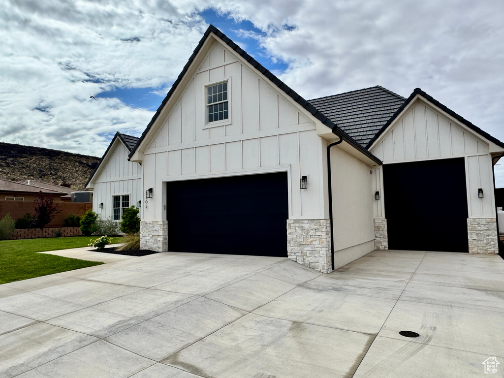 View of side of home with driveway, an attached garage, board and batten siding, and stone siding