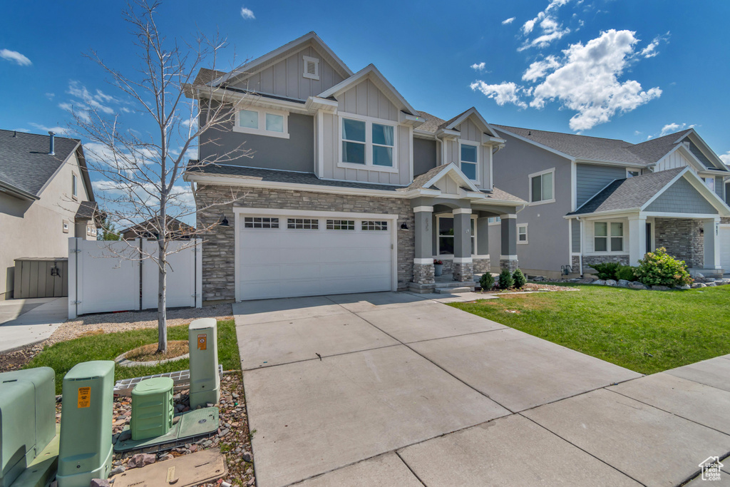 Craftsman house with board and batten siding, stone siding, driveway, a garage, and a gate