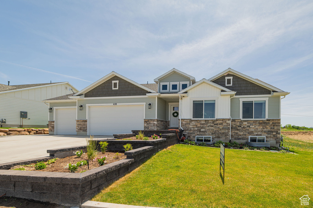 Craftsman inspired home featuring stone siding, an attached garage, a front lawn, and driveway