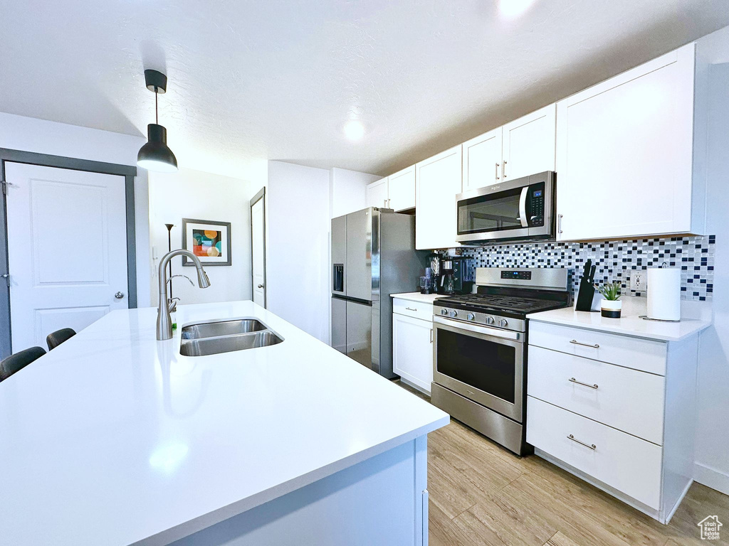 Kitchen featuring appliances with stainless steel finishes, tasteful backsplash, sink, pendant lighting, and white cabinets