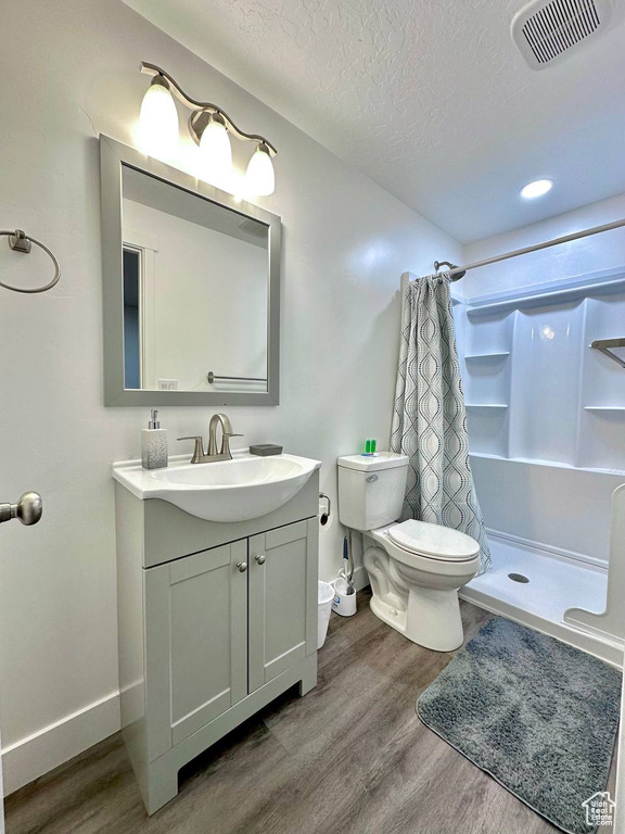 Bathroom with a shower with shower curtain, vanity, a textured ceiling, wood-type flooring, and toilet