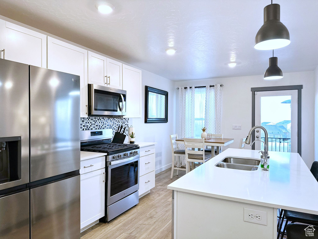 Kitchen featuring a kitchen island with sink, white cabinets, hanging light fixtures, sink, and stainless steel appliances