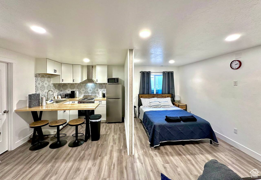 Bedroom with a textured ceiling, light wood-type flooring, sink, and stainless steel refrigerator