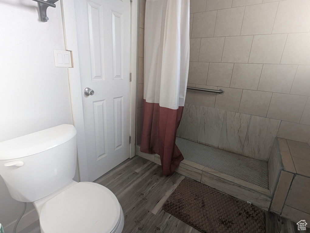 Bathroom with a shower with curtain, hardwood / wood-style floors, and toilet
