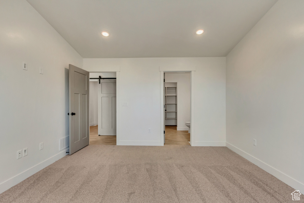 Unfurnished bedroom featuring light carpet, a walk in closet, a closet, and a barn door