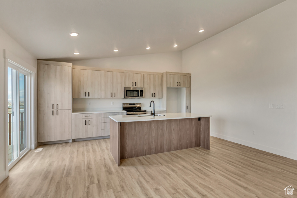 Kitchen featuring light brown cabinetry, stainless steel appliances, sink, light hardwood / wood-style flooring, and an island with sink