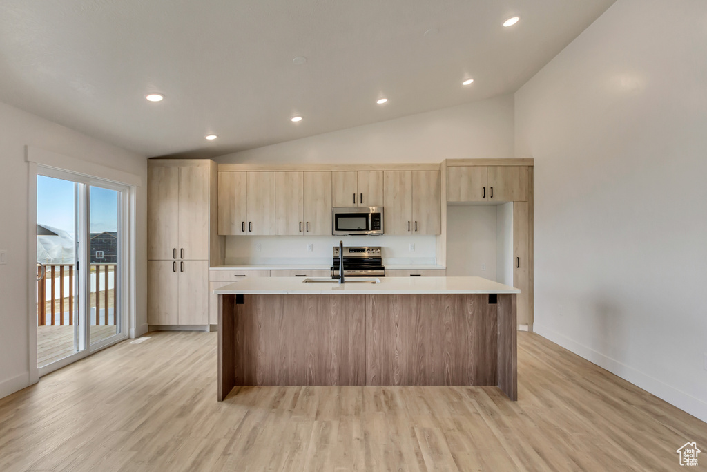 Kitchen featuring light brown cabinets, stainless steel appliances, light hardwood / wood-style flooring, and an island with sink