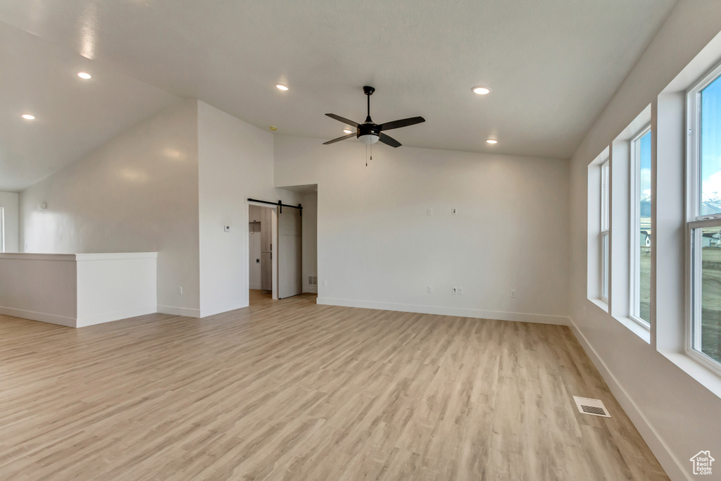 Spare room featuring ceiling fan, a barn door, a wealth of natural light, and light hardwood / wood-style flooring