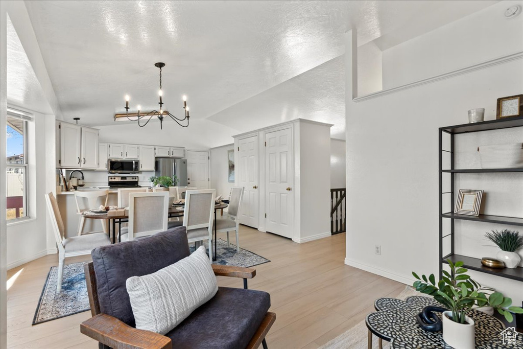 Living room with sink, light hardwood / wood-style floors, lofted ceiling, and an inviting chandelier