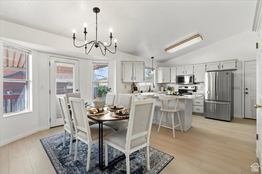 Dining room featuring sink, an inviting chandelier, vaulted ceiling, and light wood-type flooring